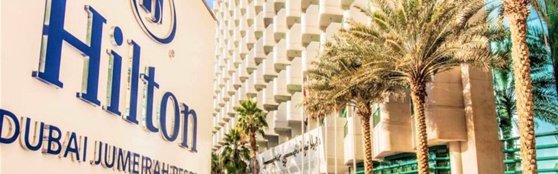 Marco Polo - Hilton Dubai Jumeirah Beach - Exteriér hotelu Hilton Dubai Jumeirah Beach na promenádě JBR v Dubaji s palmami a výhledem na moderní městské panorama.