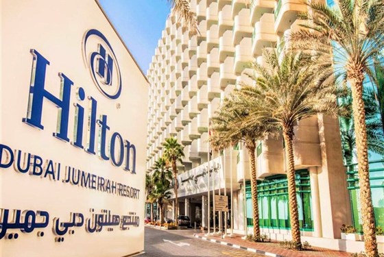Marco Polo - Hilton Dubai Jumeirah Beach - Exteriér hotelu Hilton Dubai Jumeirah Beach na promenádě JBR v Dubaji s palmami a výhledem na moderní městské panorama.