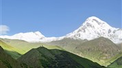 Gruzie s turistikou nejen po Kavkazu - Hora Kazbek pokrytá sněhem s klášterem Gergeti Trinity Church na zeleném hřebeni, Gruzie