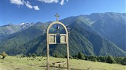 Gruzie s turistikou nejen po Kavkazu - Pravoslavný kovový kříž se zvonkem s výhledem na zelená svanetská pohoří a pasoucí se dobytek, Gruzie