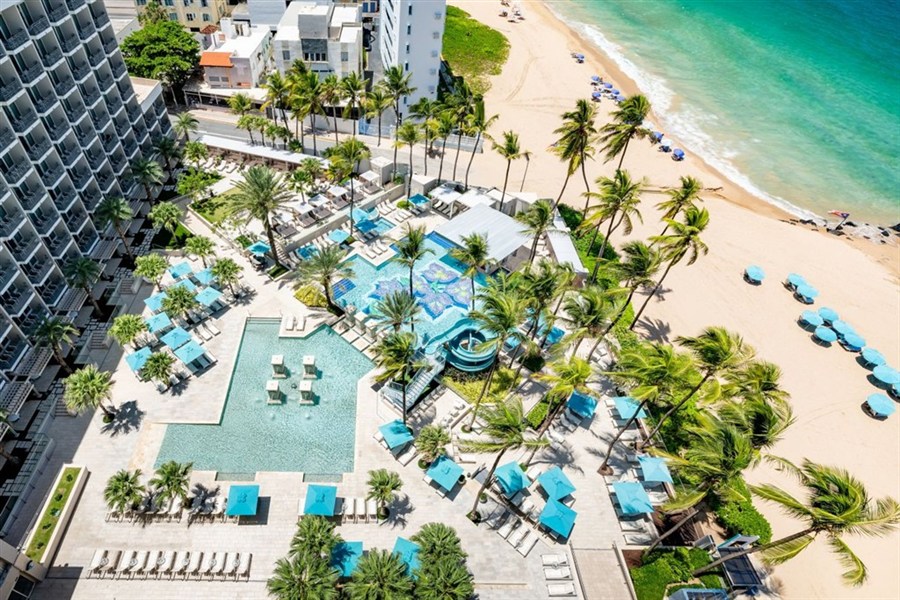 San Juan Marriott Resort & Stellaris Casino - Pohled na San Juan Marriott Resort & Stellaris Casino s bazénovým areálem, palmami a polohou u pláže Condado Beach v San Juanu.